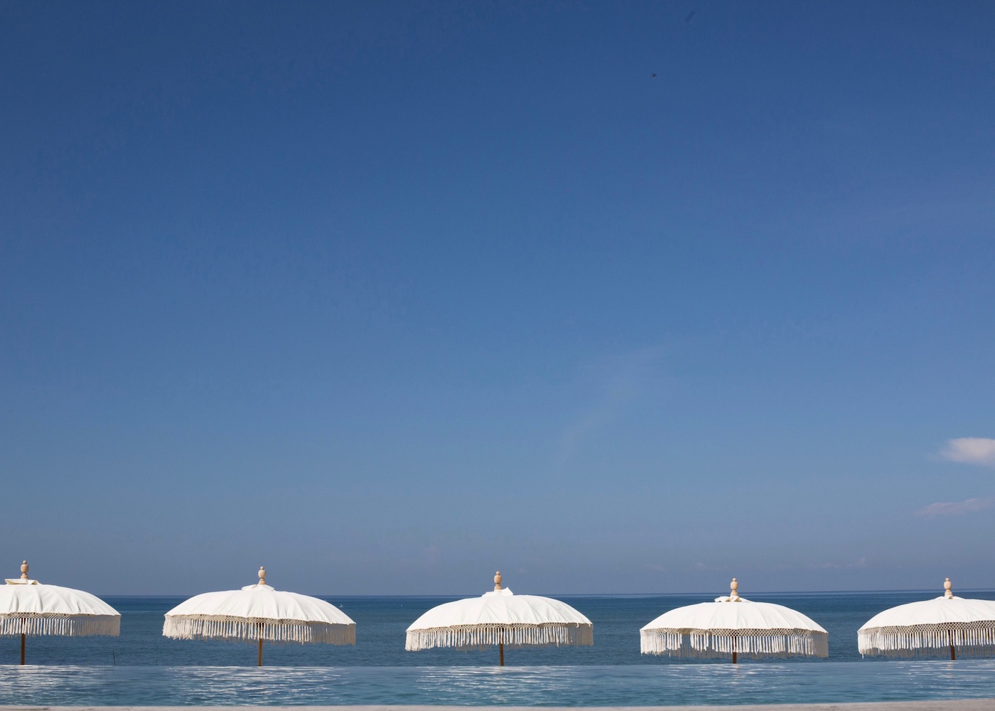 White umbrellas and infinity pool overlooking the ocean at The Lawn beach club in Canggu, Bali, Indonesia