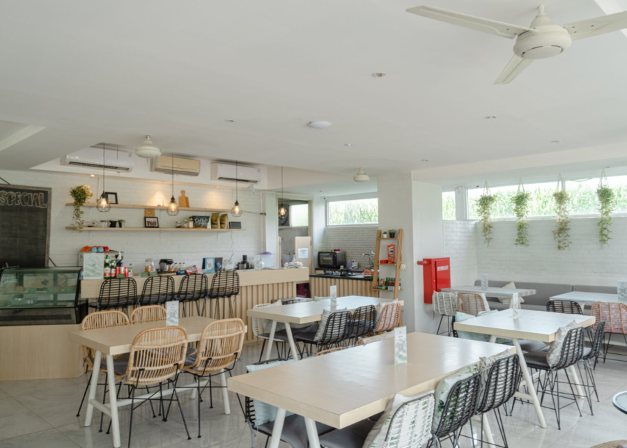 The bright, air-conditioned Bustle Cafe at Bali Bustle coworking in Kuta, with rattan chairs, white tables and rice-field views through the windows.