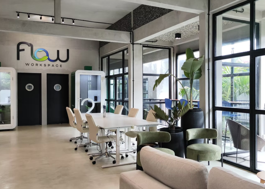 The interior of FLOW Workspace coworking in Sanur, with a white meeting desk, ergonomic chairs, phone booths and floor-to-ceiling windows onto a green balcony.