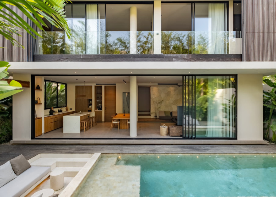 Modern two-storey villa at LAGO Villas Uluwatu featuring an open-plan living area, floor-to-ceiling glass doors and a private swimming pool surrounded by tropical greenery.