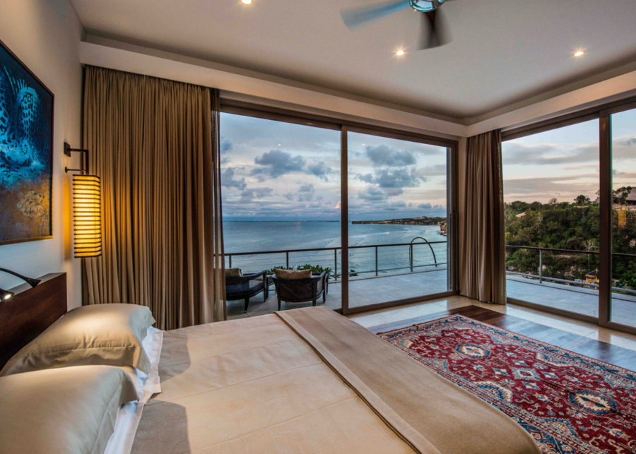Ocean-view bedroom at The Luxe Bali Uluwatu featuring floor-to-ceiling glass doors, a private balcony and sweeping views over Padang Padang Beach.