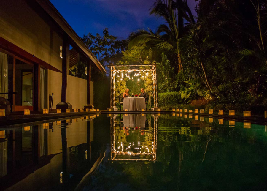 Couple enjoying a candlelit dinner beside a private pool at Ametis Villa Canggu, surrounded by lanterns and tropical greenery at night.