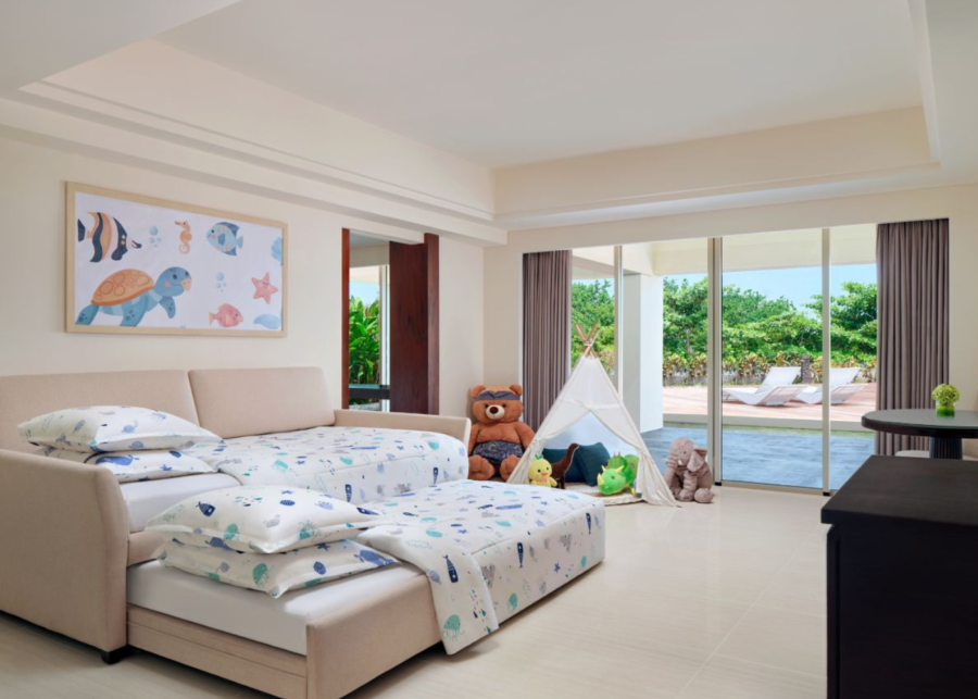 A kids' room at Sheraton Bali Kuta Resort with ocean-themed bedding, a white play teepee, stuffed animals, and sliding doors opening to a pool.