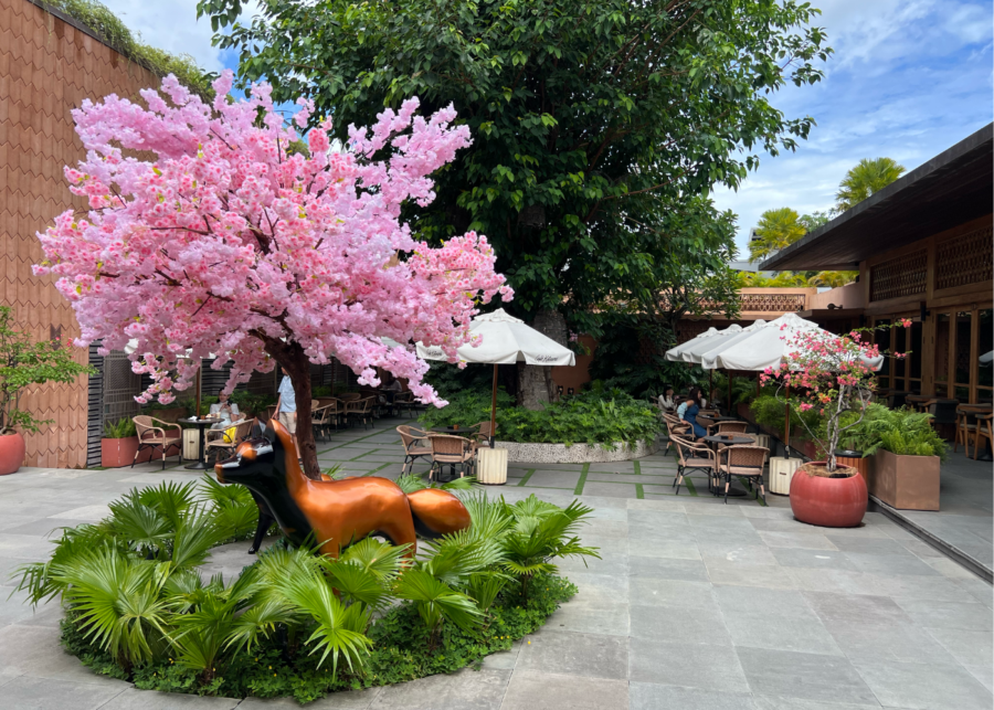 Desa Kitsune courtyard in Canggu with a pink blossom tree, fox sculpture, garden seating and outdoor dining area.