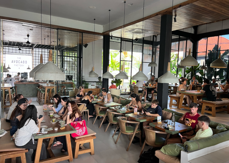 The Avocado Factory Canggu interior with wooden tables, hanging pendant lights, and diners enjoying meals in a bright, modern space.