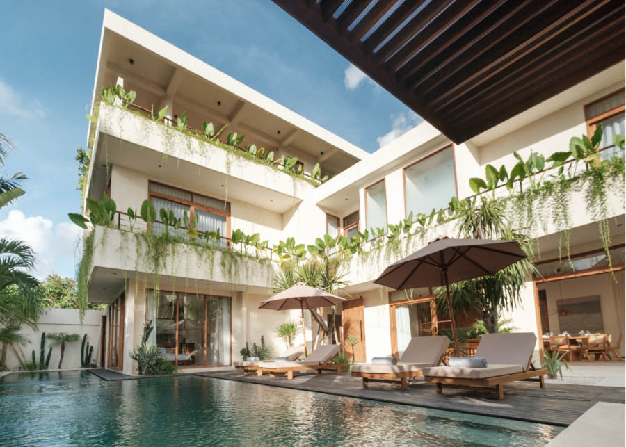 Outdoor pool deck at Manu Villas in Sanur, Bali, with four sun loungers, two umbrellas and a plant-draped villa facade.