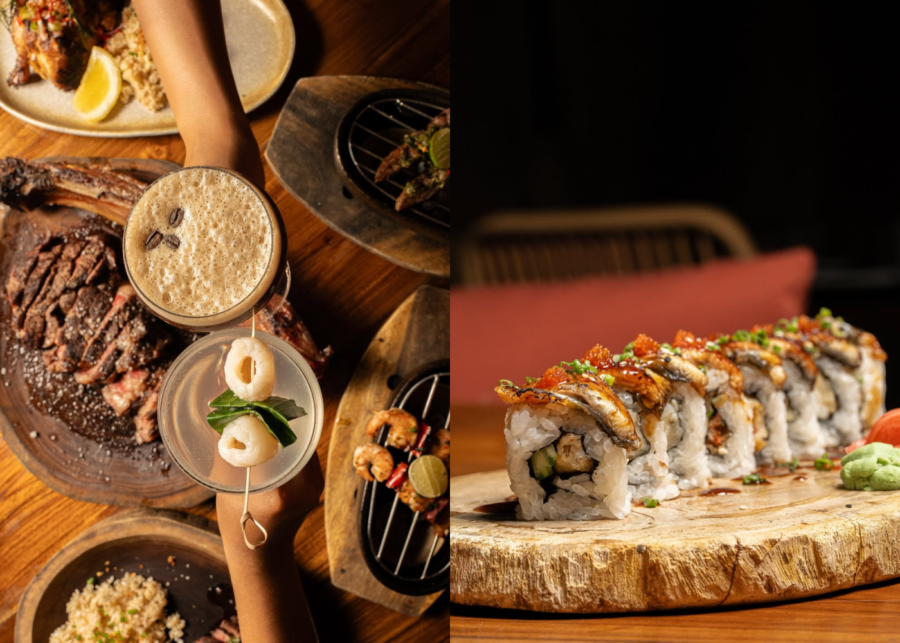 A Tabu Uluwatu spread on a dark dinner table: an eel-topped sushi roll on a wood slab, with grilled skewers, sliced steak and two cocktails.