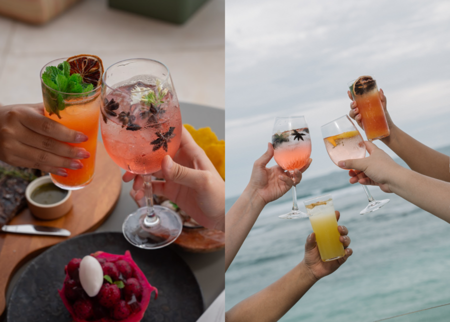 Hands raising colourful cocktails garnished with citrus and herbs over the ocean at Uma Beach House on Melasti Beach