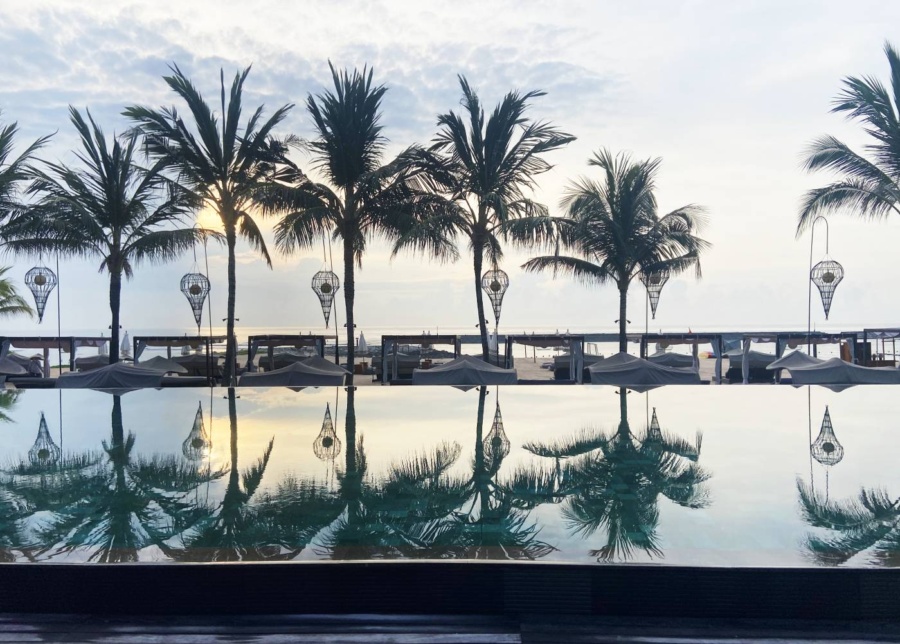 Infinity pool and palm trees overlooking sunrise at Reef Beach Club in Nusa Dua, inside The Apurva Kempinski Bali, Indonesia