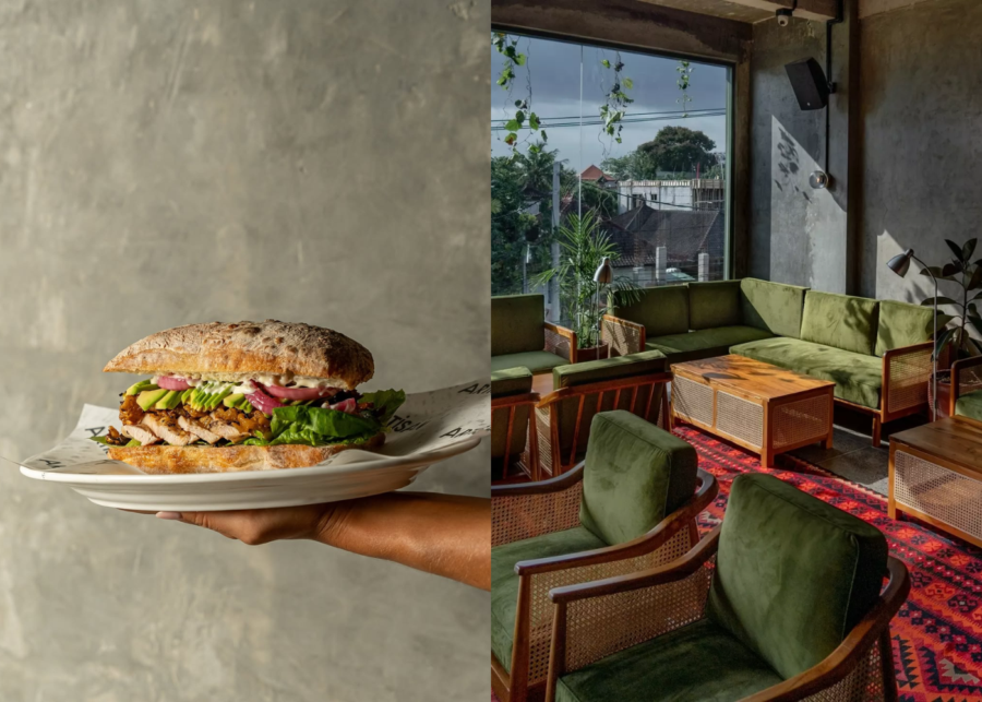 A chicken and avocado ciabatta on an Artisan-branded plate held against a concrete wall, beside a green velvet lounge area with a patterned rug at Artisan in Bingin.