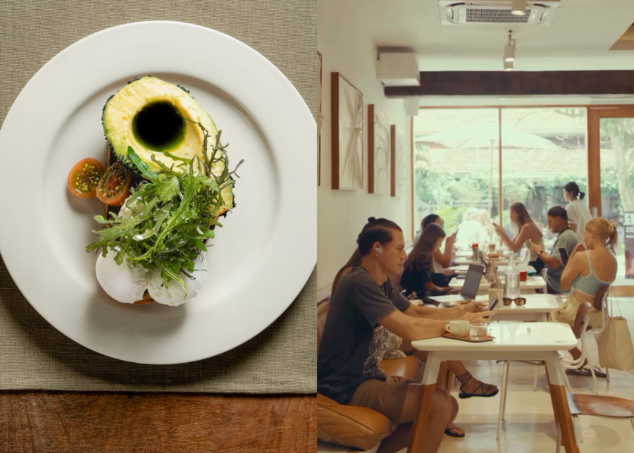 An avocado and poached egg breakfast plate topped with rocket at BAKED. in Uluwatu, beside an air-conditioned room of people working on laptops at white tables by a garden window.