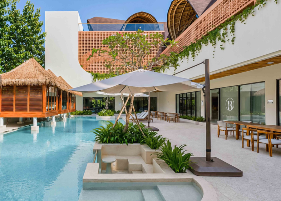 Pool courtyard with thatched-roof pavilions and dining tables at BWork Uluwatu coworking space.