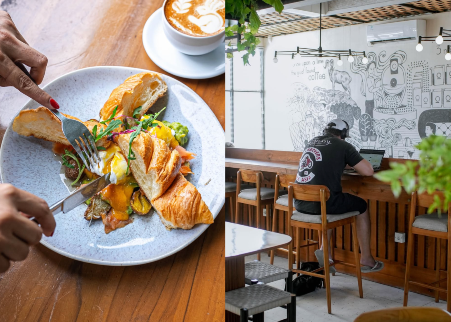 A croissant eggs benedict and a latte on a wooden table at Fine by Satu Satu in Canggu, with a person working on a laptop at the bar seating beneath a coffee mural.