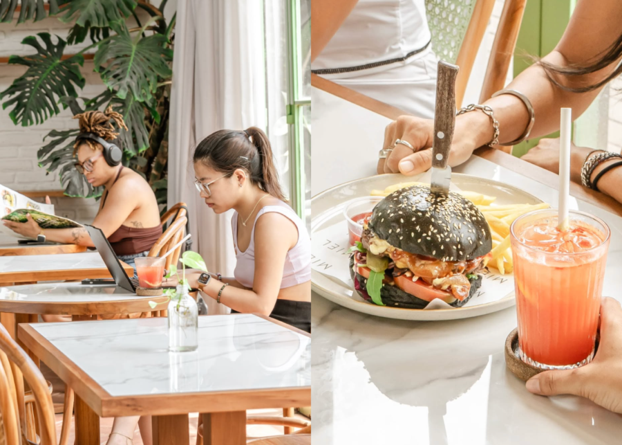Two people working on a laptop and reading beside big monstera plants at Miel Specialty Coffee in Canggu, next to a black bun burger and a fresh juice.