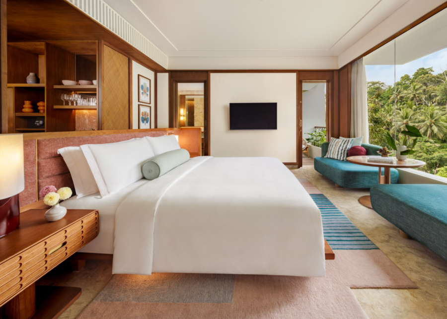 Essential Room at Kimpton Suntaya Bali Ubud with pink upholstered headboard, teal sofa, and floor-to-ceiling window overlooking jungle.