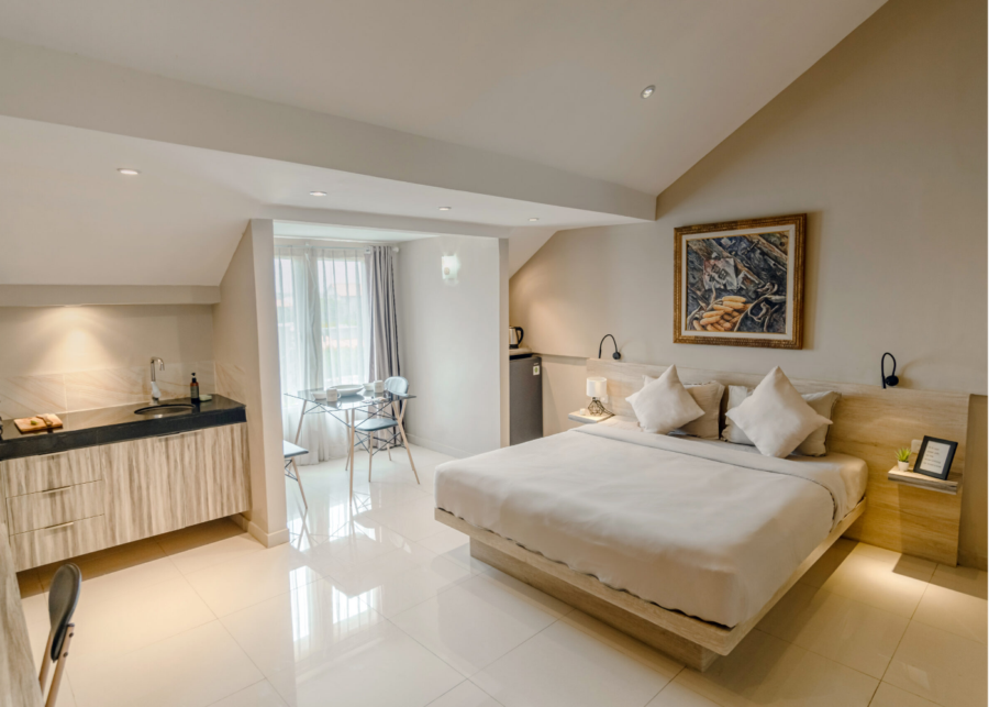 A bright loft room at Bali Bustle coliving in Kuta, Bali, with a double bed, a kitchenette and a small dining table by the window.