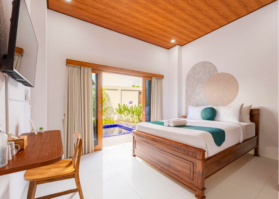 A private room at Cove Abasan coliving in Canggu, Bali, with a wooden ceiling, a work desk and sliding doors opening onto a small pool.