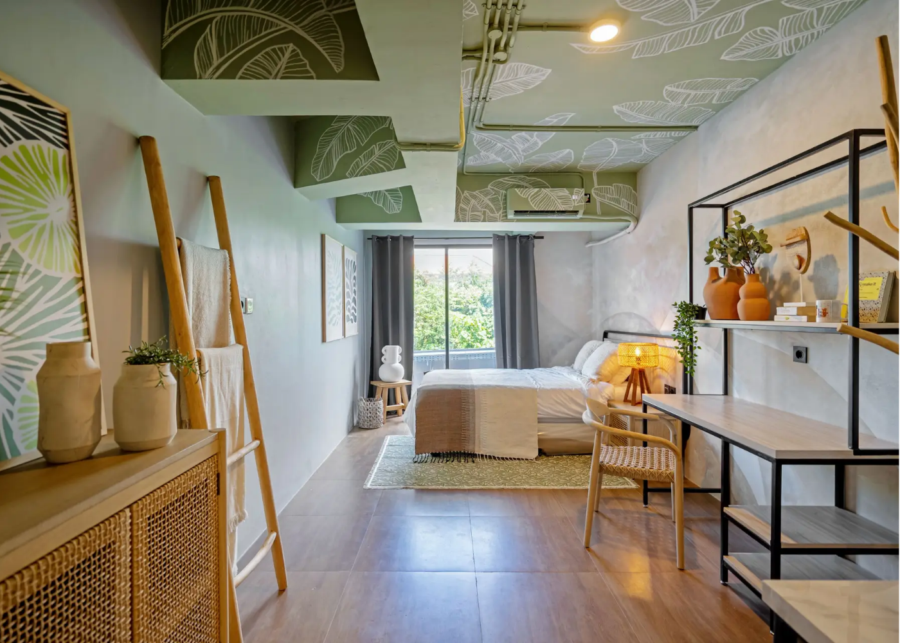 A studio at Rukita Sunset Road coliving near Seminyak, Bali, with a leaf mural ceiling, a double bed, a work desk and shelving.