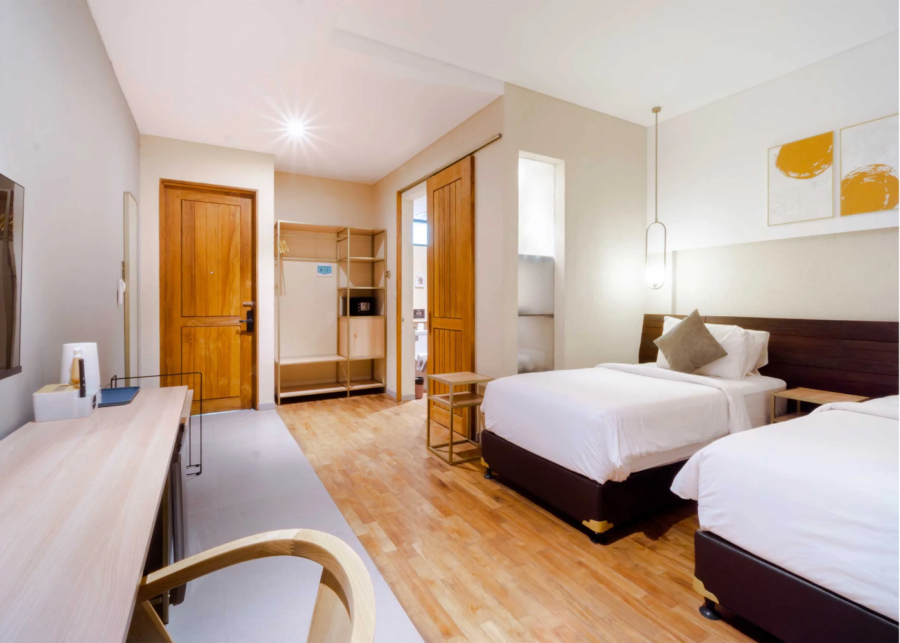 A twin room at Tanaga coliving in Seminyak, Bali, with two single beds, a long work desk and open shelving.