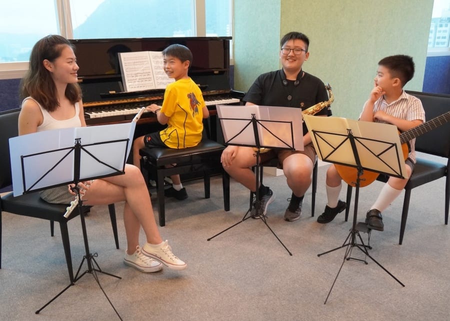 teachers sitting with students to learn to play guitar, piano, and clarinet