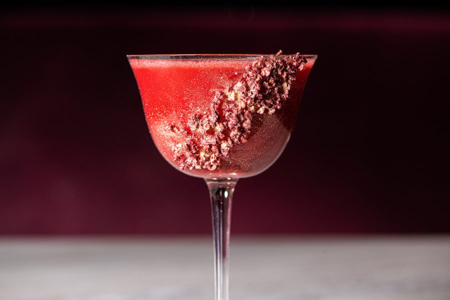 a pink drink in a glass with dried raspberries on the glass